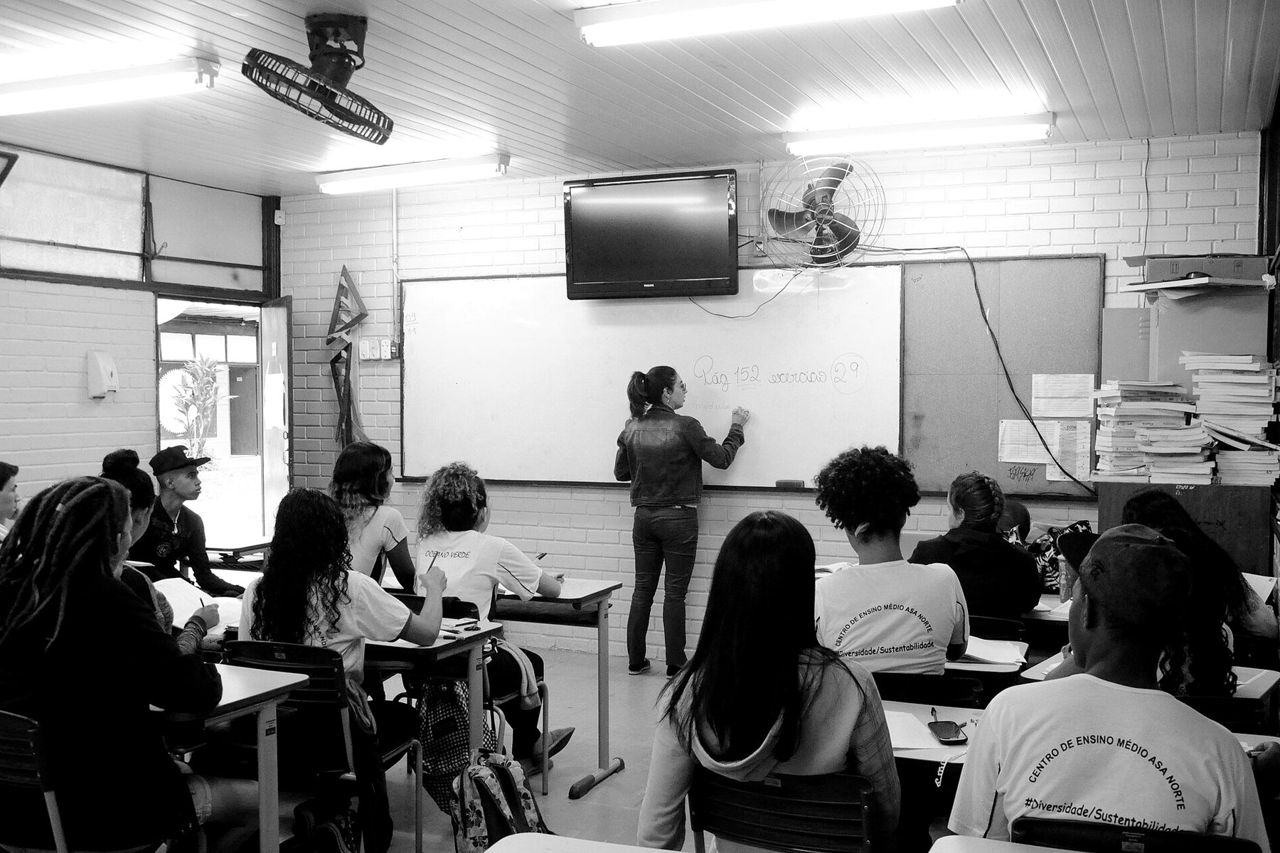 Turma de ensino médio em sala de aula, professora escrevendo no quadro, em preto e branco